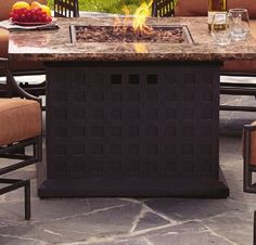 a fire pit sitting on top of a stone patio next to chairs and table with fruit