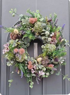 a wreath with flowers and greenery hanging on the front door to decorate it for someone's special occasion