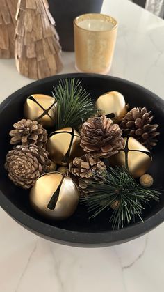 a bowl filled with golden ornaments and pine cones on top of a white marble table