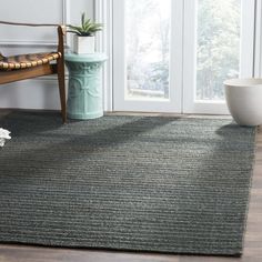 a room with a chair, vase and rug on the floor in front of a window