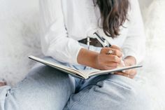 a woman sitting on a couch holding a pen and paper in her lap while writing