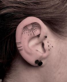 a woman with black dots on her ear has a sun and stars tattoo behind the ear