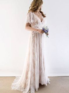 a woman in a white dress holding a bouquet of flowers and looking at the wall