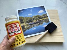 a hand holding a bottle of glue next to a photo on a wooden board with a rubber stamp