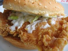 a fried chicken sandwich with lettuce and mayonnaise on a sesame seed bun