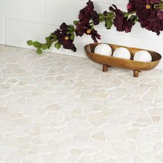 three white balls in a wooden bowl on a marble counter top next to purple flowers