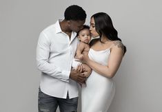 a man and woman holding a baby while standing next to each other in front of a gray wall