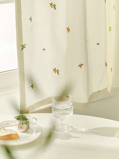 a white table topped with a plate of food next to a window covered in curtains