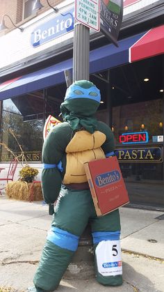 a statue of a man dressed as a turtle holding a pizza box on the sidewalk