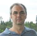 a man with glasses and a blue shirt is posing for a photo in front of some trees