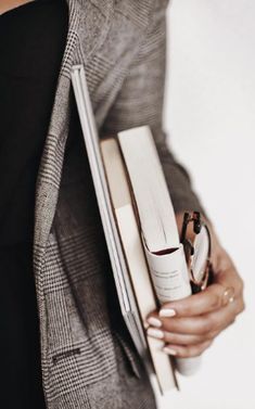 a woman is holding two books and a watch in her hand while wearing a gray blazer