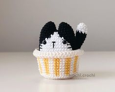 a small crocheted cat sitting in a cupcake with black and white stripes