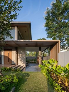 the house is surrounded by lush green plants and trees, with a walkway leading up to it