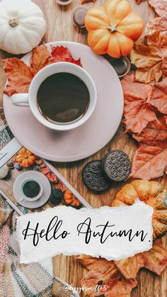 a cup of coffee sitting on top of a table next to autumn leaves and cookies