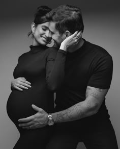 a black and white photo of a pregnant couple hugging each other with their arms around one another