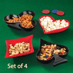 four heart shaped bowls filled with different types of candy and snacks on a green table