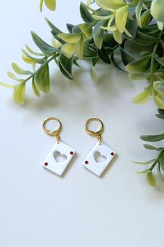 two white square shaped earrings sitting on top of a table next to green leaves and flowers