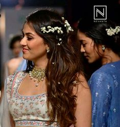 a woman with long hair wearing a white dress and flower in her hair, standing next to other women