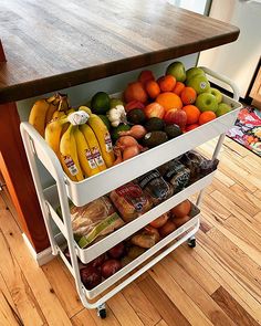 a cart filled with assorted fruit on top of a hard wood floored kitchen