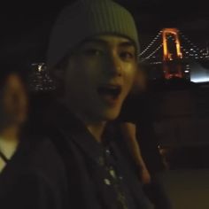 a man standing in front of a bridge at night with his mouth open and tongue out