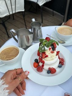 a person is pointing at a dessert on a table with two cups of coffee in the background