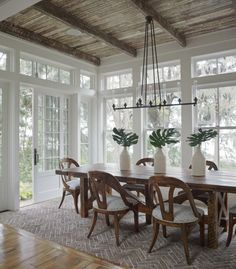 a dining room table with chairs and vases on it in front of large windows