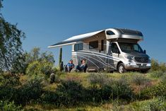 two people are sitting in front of an rv parked on the side of a hill