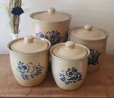 four blue and white canisters sitting on top of a wooden table next to a vase