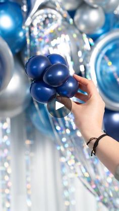 a person holding blue balloons in front of some silver and blue balls on a wall