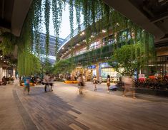 many people are walking around in an open area with greenery hanging from the ceiling