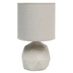 a white table lamp with a beige shade on the base and a light bulb in front of it