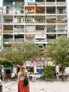 a woman is walking down the street in front of a building with many balconies