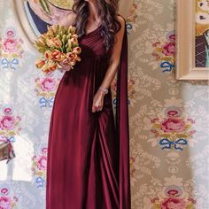 a woman standing in front of a floral wallpaper holding a bouquet of flowers and smiling