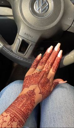 a woman's hand with henna on her arm sitting in front of a steering wheel