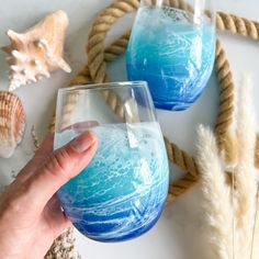 someone holding a wine glass with blue liquid in front of some sea shells and seashells