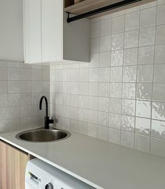 a kitchen with white tile and wood cabinets, a washer and dryer in the corner