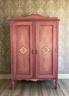 an old pink armoire with ornate carvings on the doors and handles, against a wallpapered background