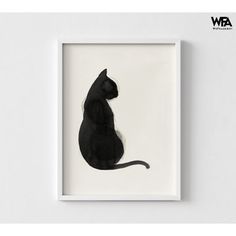 a black cat sitting on top of a white wall next to a framed photo in a frame