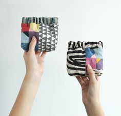 two hands are holding small bags with designs on them, one is multicolored and the other is black and white