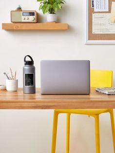 a laptop computer sitting on top of a wooden desk next to a yellow chair and potted plant