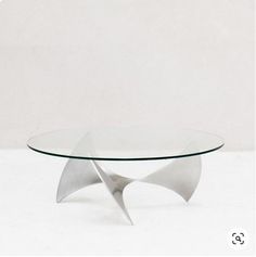 a glass and metal coffee table with an abstract design on it's base, against a plain white background