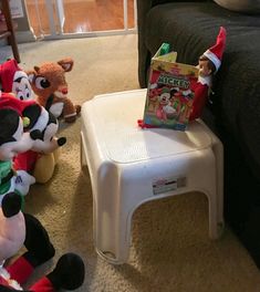 several stuffed animals sitting on the floor in front of a chair with a christmas book