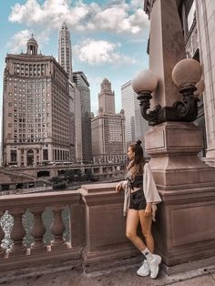 a woman leaning against a pole on the side of a bridge with buildings in the background