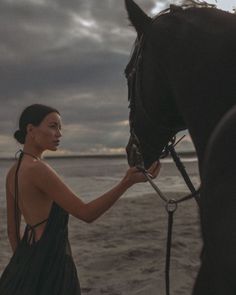 a woman standing next to a horse on the beach