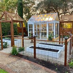 an outdoor garden with a greenhouse in the center and several plants growing inside, along with brick walkway