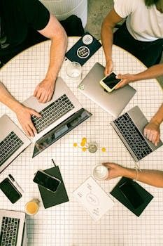 four people sitting at a table with laptops on top of each other in a circle