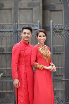 a man and woman standing next to each other in front of an iron gate wearing red outfits