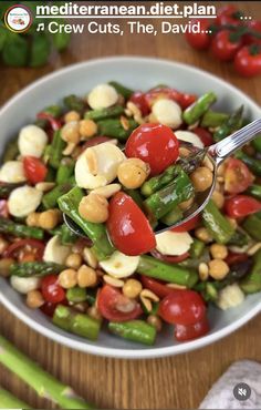 a white bowl filled with green beans, tomatoes and other veggies on top of a wooden table