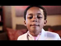 a young boy wearing a white suit and pink tie looking at the camera with his eyes closed