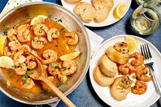 a pan filled with shrimp next to bread and lemon wedges on top of a table